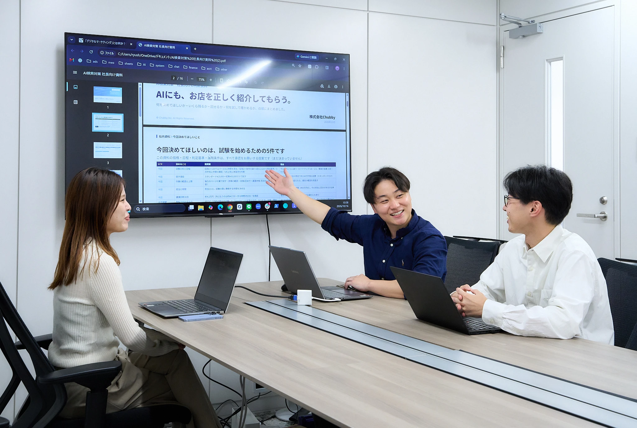 会議室のモニターで資料を説明する社員と、話を聞くメンバー