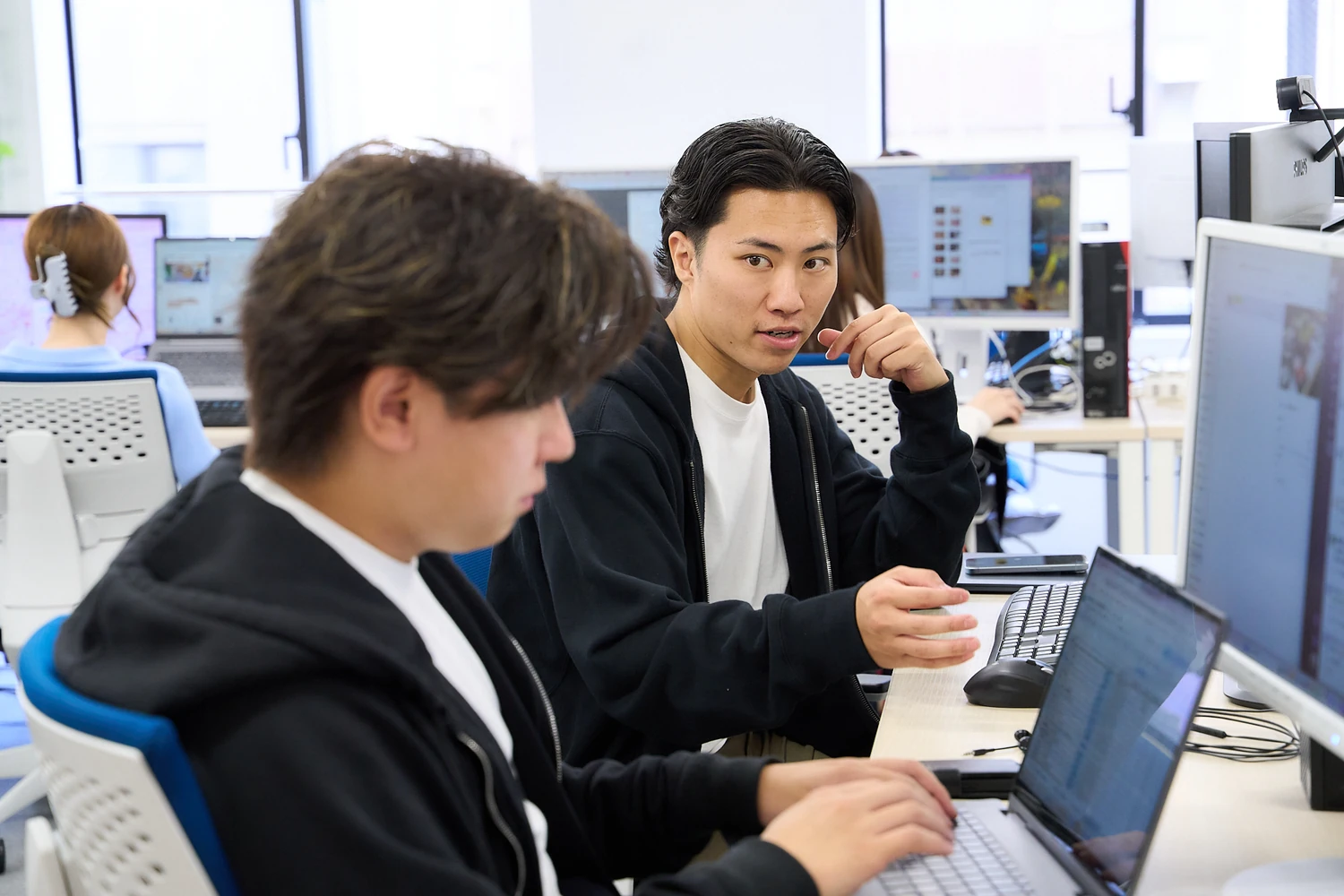 隣の席で話しながら作業する社員